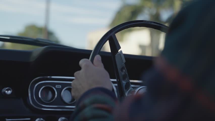 Man driving classic convertible vintage car - close up on steering wheel. Right side car steering driving down a sunny street in Australia with beautiful old vehicle. Hands turn the car wheel