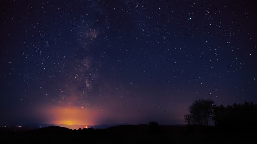 Milky Way stars with meteor shower trails and countryside silhouettes. Timelapse video.