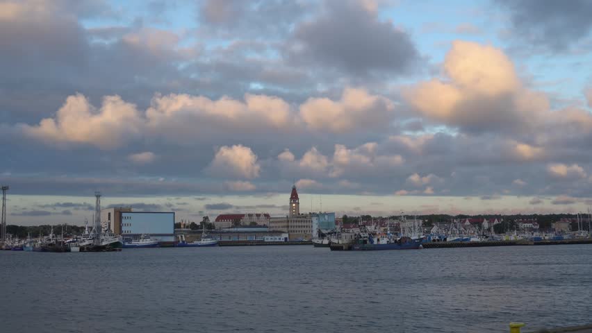 Wide view of Władysławowo harbor with boats and buildings, under a cloudy sky during dusk by the Baltic Sea.