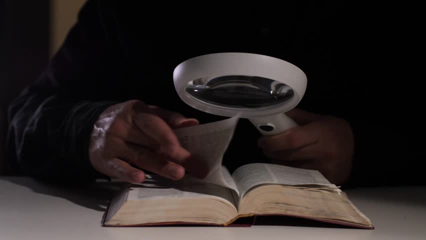 Person reading book with magnifying glass in dark room