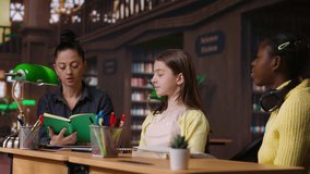 Elementary students receiving support from a tutor working on homework assignments in a diverse learning environment in the school library. Professor guiding her pupils before class. Camera B. - Powered by Shutterstock - Get 15% off with code: PIKWIZARD15