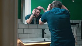 A man stands in front of a bathroom mirror, looking worriedly at his hair, checking for signs of hair loss. - Powered by Shutterstock - Get 15% off with code: PIKWIZARD15