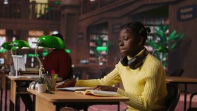 Young focused scholar doing her homework at a library desk after classes, engrossed in literature and notes. Pupil completing her notes in the copybook, productive study sessions. Camera B. - Powered by Shutterstock - Get 15% off with code: PIKWIZARD15