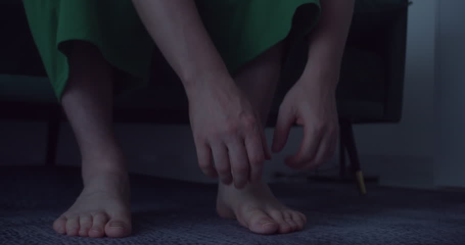 Guy is rubbing his foot 'cause his feet because of painful attack. Mature man with arthritis is sitting on the bed, rubbing his ankle and foot to alleviate pain.