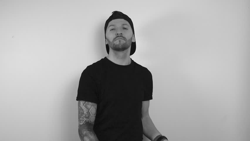 Grayscale footage of a tattooed man with black clothing raising or lifting up a concrete model of a bitcoin coin in slow motion while being happy and nodding with approval in front of a white back