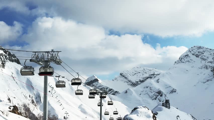 Ski lift in ski resort in winter. Snow-covered mountains and the blue sky with clouds. Winter landscape. Krasnaya polyana, Sochi, Russia. 
