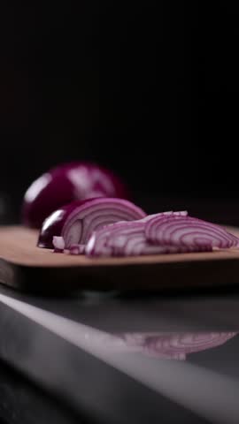 Vertical closeup slow-motion of slicing onion with a kitchen knife on the wooden cutting board