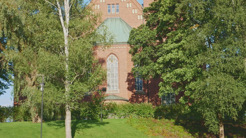 Historic Lutheran church spire in Forssa, Finland with red brick facade and copper steeple. Beautiful architectural landmark surrounded by birch trees against bright blue summer sky
