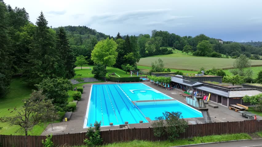 Aerial view circling leisure swimming pool with diving board in luxury Swiss vacation resort