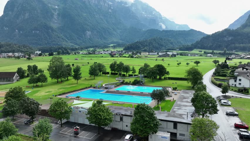 Aerial view establishing swimming pool and water slide under Swiss mountains vacation town landscape