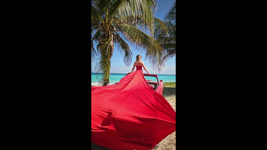 eautiful young woman with blond brunette hair in red fluttering dress on the coastline of azure caribbean sea