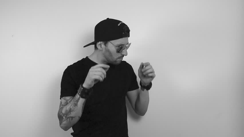 grayscale footage of a tattooed man having aviator sunglasses on and looking at something in such disbelief that he takes glasses off and begins to shake his head in slow motion and look to the side.