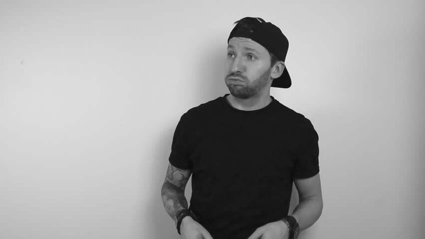 grayscale footage of a tattooed man having aviator sunglasses on and looking at something in such disbelief that he takes glasses off and begins to shake his head in slow motion and look to the side.