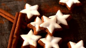 Close-up of a hand picking a Christmas star cookie with white icing. The cookies rest on a rustic surface with cinnamon sticks, creating a warm and festive holiday atmosphere. - Powered by Shutterstock - Get 15% off with code: PIKWIZARD15