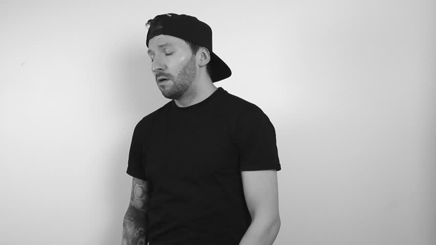 Grayscale footage of a tattooed man feeling unwell and sick from covid, bird flu or regular flu and blows his nose into a white tissue in slow motion making it move with the air coming out of his nose