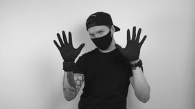 Grayscale footage of a tattooed man putting on black rubber or nylon protective gloves and a black face mask for health reasons. After putting them on in slow motion, man shows his hands and claps. - Powered by Shutterstock - Get 15% off with code: PIKWIZARD15