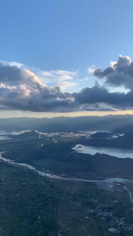 Vertical screen: A captivating aerial view of a serene landscape with winding rivers, lush green valleys, and distant mountains under a vibrant blue sky with scattered clouds.