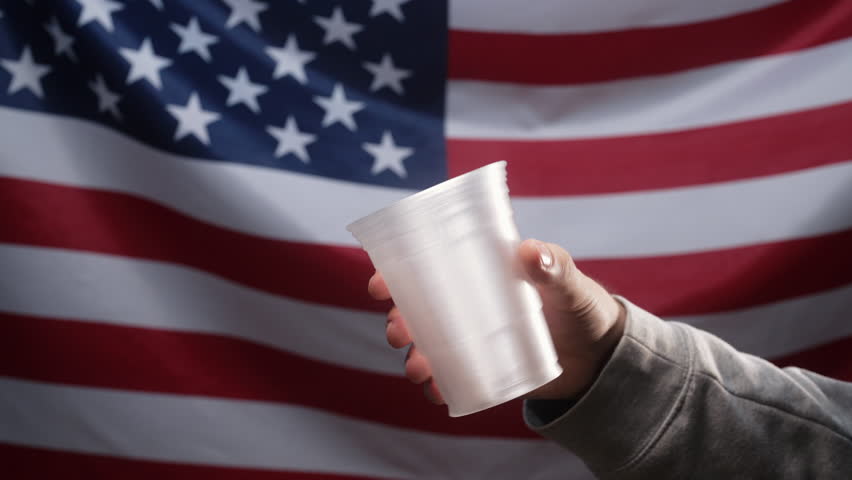 Rich american Woman Throws coins cents Into Plastic Cup Of Homeless Man Who Is Asking For alms on usa flag. Sharing and help each other. Poor life, unemployment, people below poverty line.