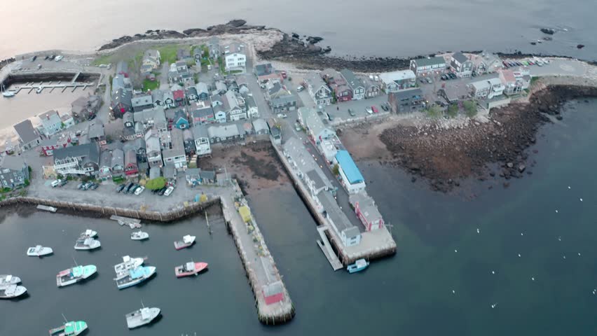Aerial Fly-By Over Rockport Waterfront with Boats, Coastal Buildings, and Rugged Shoreline