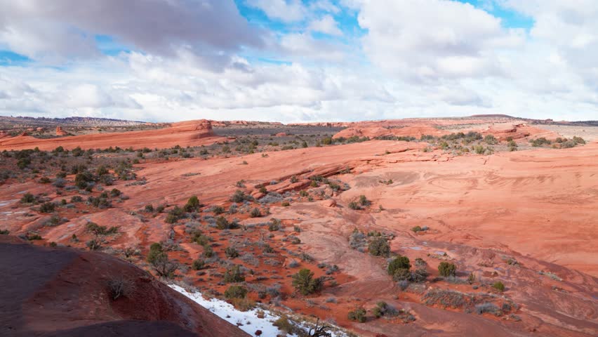 Panning shot of the red rocky mountains of Arches National Park on a sunny day with thick clouds in the sky.