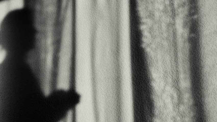 Lonely woman silhouette looking out the window. Female silhouette opens curtains.black and white depressive video. A womans shadow opens the light curtains. Melancholy mood
