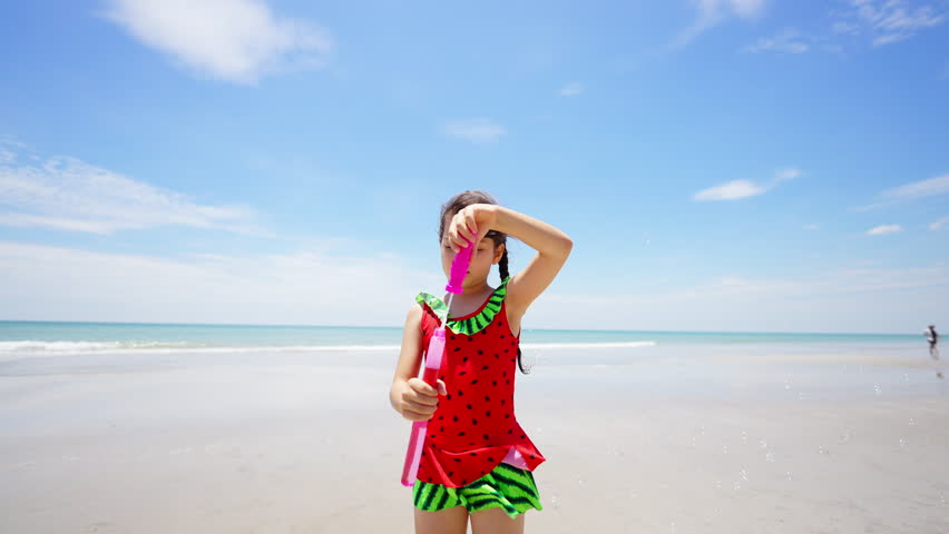 Happy Children travel playing at the sea on summer beach holiday vacation. Little cute Asian child girl kid in swimwear enjoy and fun outdoor lifestyle playing bubble wand at tropical island beach.