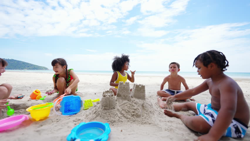Happy Children travel playing at the sea on summer beach holiday vacation. Group of Little cute child boy and girl kids enjoy and fun outdoor lifestyle playing beach toy build sand castle on the beach