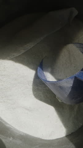 Vertical video. Tossing the blue scoop back into the pre-workout powder jar, deciding against using the supplement. Dolly slider, close up. Slow motion.