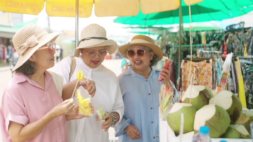 Happy Asian senior woman travel city street on summer holiday vacation. Group of Healthy elderly retired women friends enjoy and fun outdoor lifestyle shopping and eating street food at street market.