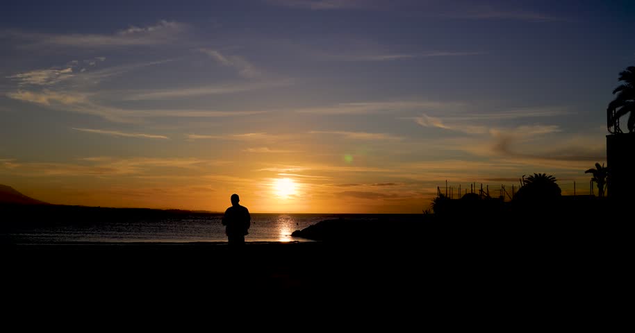 Footage of the beach front in the town or Marbella in Malaga Spain showing the beautiful sun setting over the ocean in the evening with the yellow sun reflecting on the ocean and a silhouette of a man