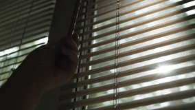 Person hand rotates handle and changes position of horizontal blinds to protect from sunlight. Silhouette of moving slats on window against background of sun rays. Protection from light and heating. - Powered by Shutterstock - Get 15% off with code: PIKWIZARD15
