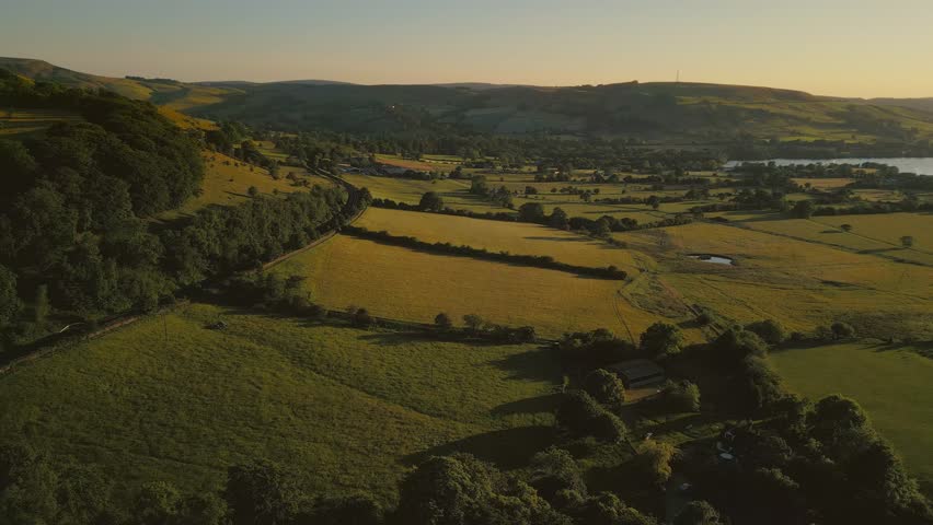 A Drone shot over green fields and hills at sunset
