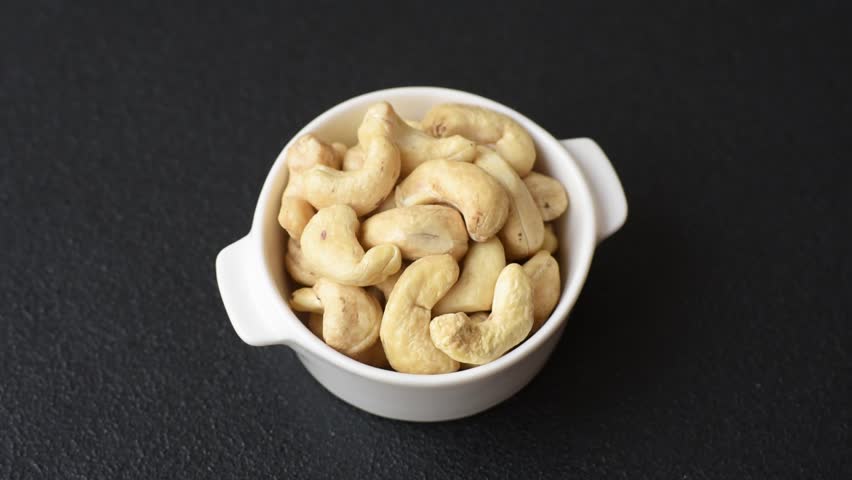 Delicious nutritious cashew nuts in ceramic bowl on dark concrete background
