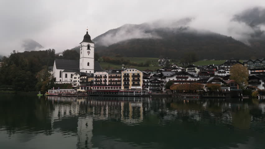 moving aerial drone close up shot of Wolfgang am Wolfgangsee on a cloudy day very close to the lake and mountains with clouds on them