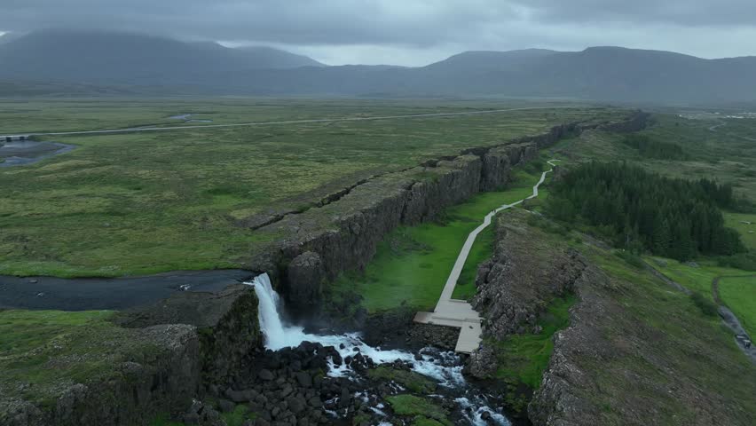 A breathtaking aerial view of Thingvellir National Park in Iceland, showcasing a cascading waterfall, tectonic rift, and lush green plains.