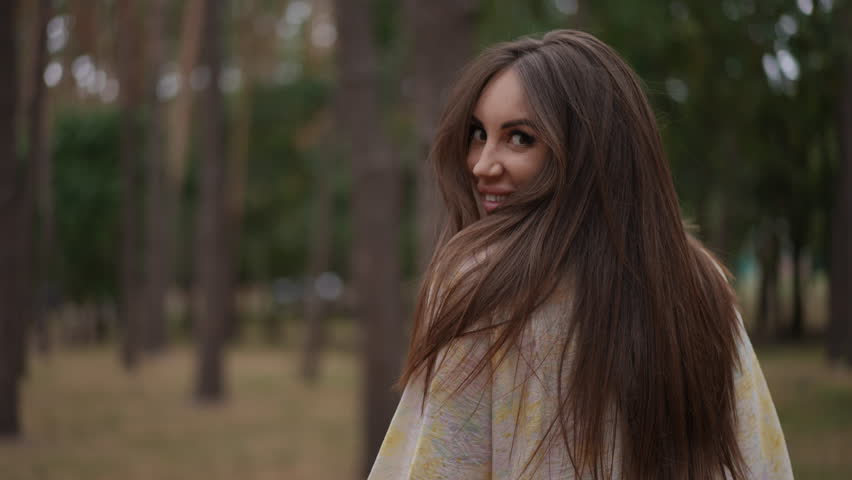 A smiling woman with vibrant, keratin-enriched hair glances back in a serene forest. Her silky, strong strands reflect optimal hair care, nourished with essential vitamins and proteins, showcasing the