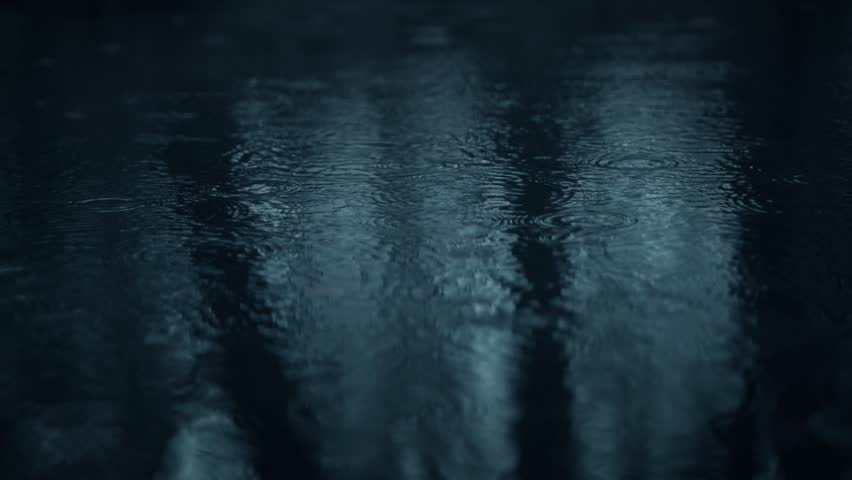 A beautifully serene closeup of numerous raindrops creating subtle ripples on a dark water surface