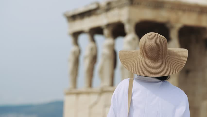 Woman with hat sightseeing Acropolis in Athens looking at Caryatid Porch on ancient Erechtheion or Erechtheum temple. It is world famous landmark at the Acropolis Hill