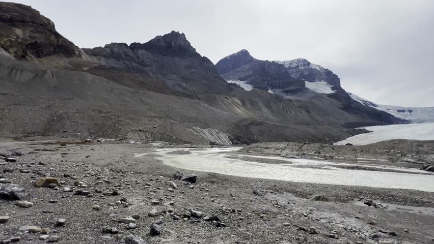 Athabasca Glacier, part of Columbia Icefield in Jasper National Park, Alberta, Canada, with icy expanse flanked by rugged, rocky peaks under cloudy sky, Canada, Panning