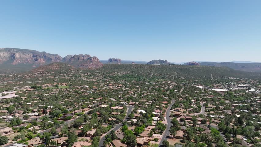 Aerial wide shot of Sedona desert City in Arizona with Main Street. American neighborhood during sunny day with blue sky. Giant red rock formation in distance.