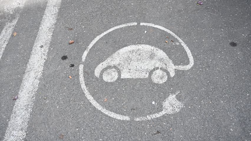 Electric car charging symbol on asphalt street in city. Hybrid and electric cars can be charged here. Charging station sign. 