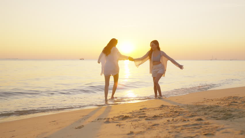 Happy woman travel nature ocean on summer beach holiday vacation. Group of Asian women friend enjoy and fun outdoor lifestyle dancing and playing in the sea together on tropical island beach at sunset
