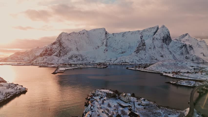 Flying over Sakrisoy towards Reine in Lofoten at dramatic sunset sky and on a calm day with light waves