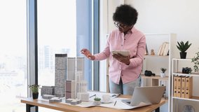 African American female architect uses digital tablet to develop and evaluate project for modern city. She stands beside architectural models in well-lit office. - Powered by Shutterstock - Get 15% off with code: PIKWIZARD15