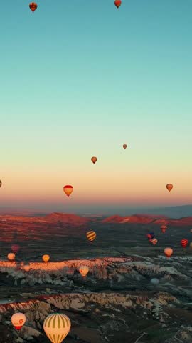 Hot air balloons with tourists hanging and flying in the blue sky above a valley of cliffs. Cappadocia, Turkey
