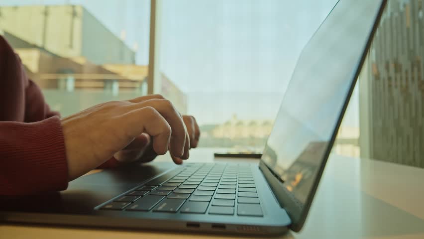 A Close-Up Of Hands Typing Code On A Laptop Keyboard In A Coworking Space. The Developer Focuses On Work, With The Office Environment Creating An Ideal Space For Productivity.