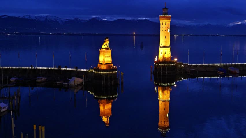 Harbor of Lindau on lake Constance with illuminated lighthouse and lion statue at evening, Germany, Bavaria