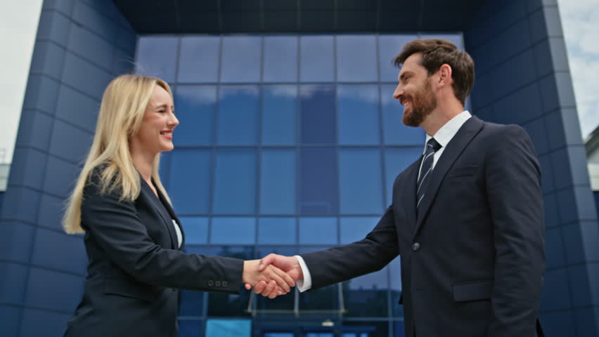 Closeup business people handshake in front modern office building. Confident businessman businesswoman shaking hands during business interaction outdoors. Professional partners initiating agreement