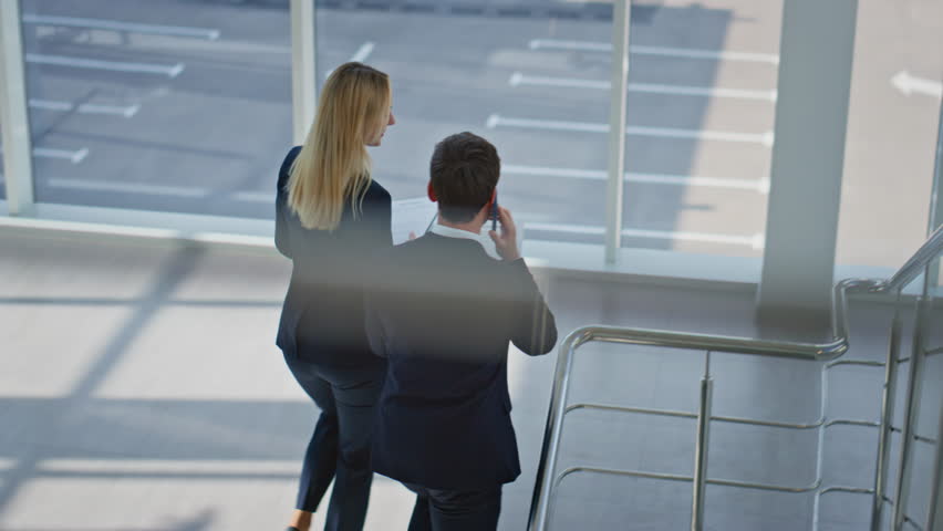 Business partners discussing documents walking up stairs modern office building. Calling businessman reviewing papers from businesswoman. Corporate colleagues climbing staircase talking together. - Powered by Shutterstock - Get 15% off with code: PIKWIZARD15