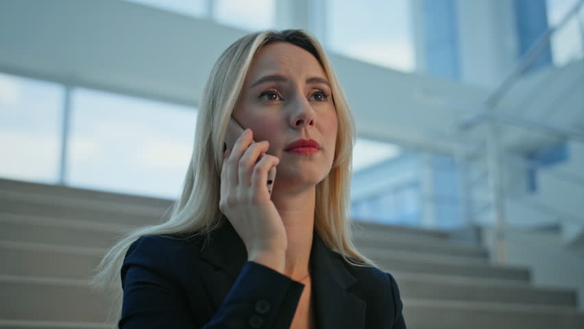 Stressed business lady calling mobile phone with tense expression closeup. Frustrated businesswoman talking cellphone holding document on office stairs. Upset woman worried report speaking smartphone.